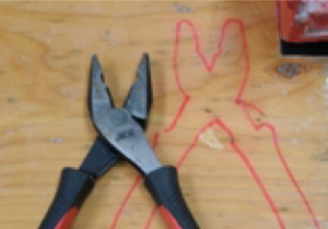 A pliers is sitting on a wooden table top just out of line with an outline of the same item.