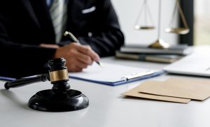 Person holding a pen and signing a document at a desk with a gavel on one side and scales on their other.