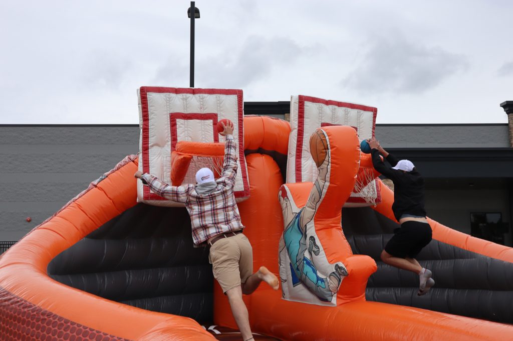 Two people jumping up and dunking basketballs at the same time on an inflatable basketball court.